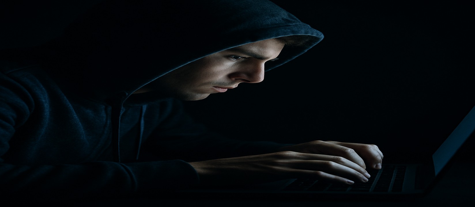 একজন ব্যক্তি অন্ধকারে ল্যাপটপে বসে, মনোযোগী চেহারা নিয়ে 6zz ওয়েবসাইটে অনলাইন গেম খেলছেন